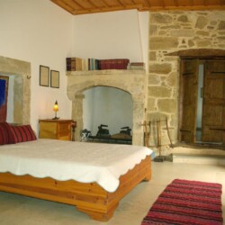 Master bedroom of Sior Nikoletos with a double bed and a traditional Cretan rug, blending comfort and rustic charm