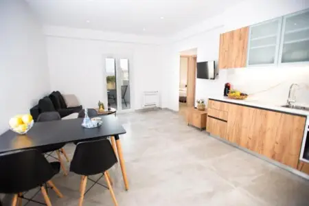 Modern living area with kitchen on the right, dining area with black table and chairs on the left, and a cozy couch